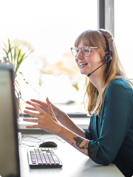 Woman with glasses and a headset talking animatedly on a web call.