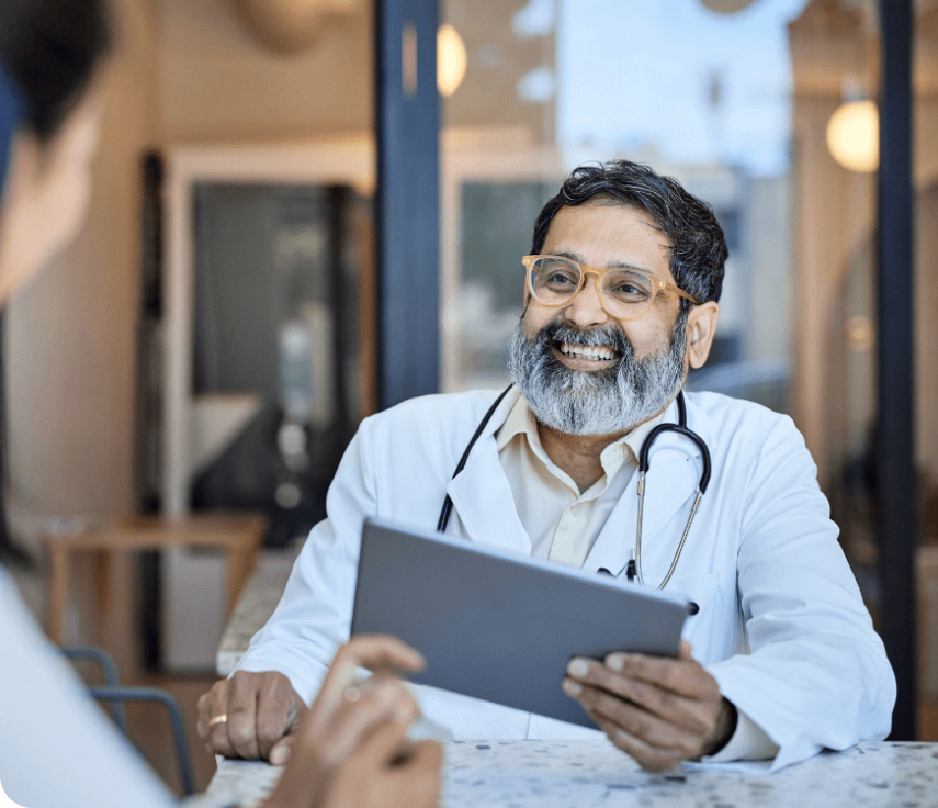 Smiling doctor with yellow glasses and a gray beard holds tablet