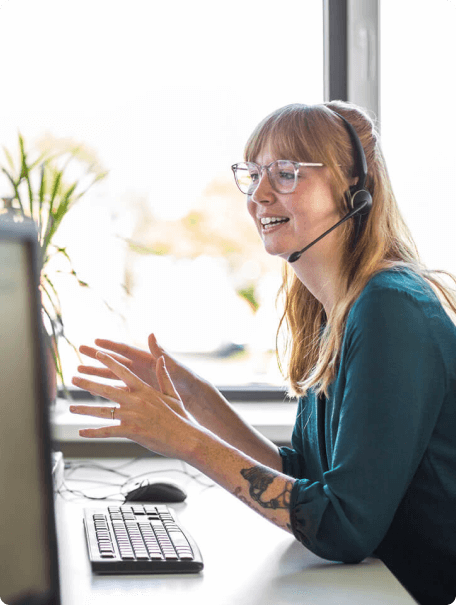 Woman with reddish hair and a headset talks animatedly on a virtual call